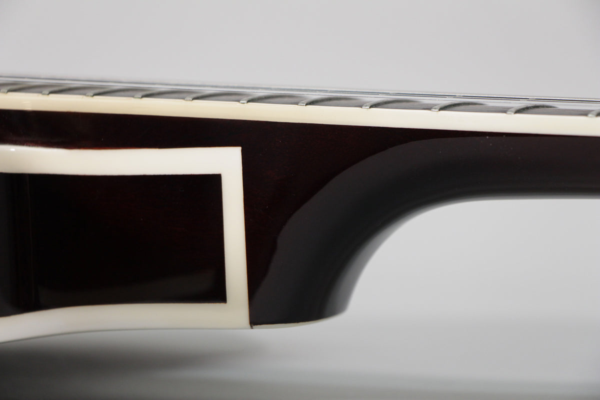 Close-up of the guitar's dark brown neck heel and lower fretboard, showing cream binding and a small rectangular cutout on the body.