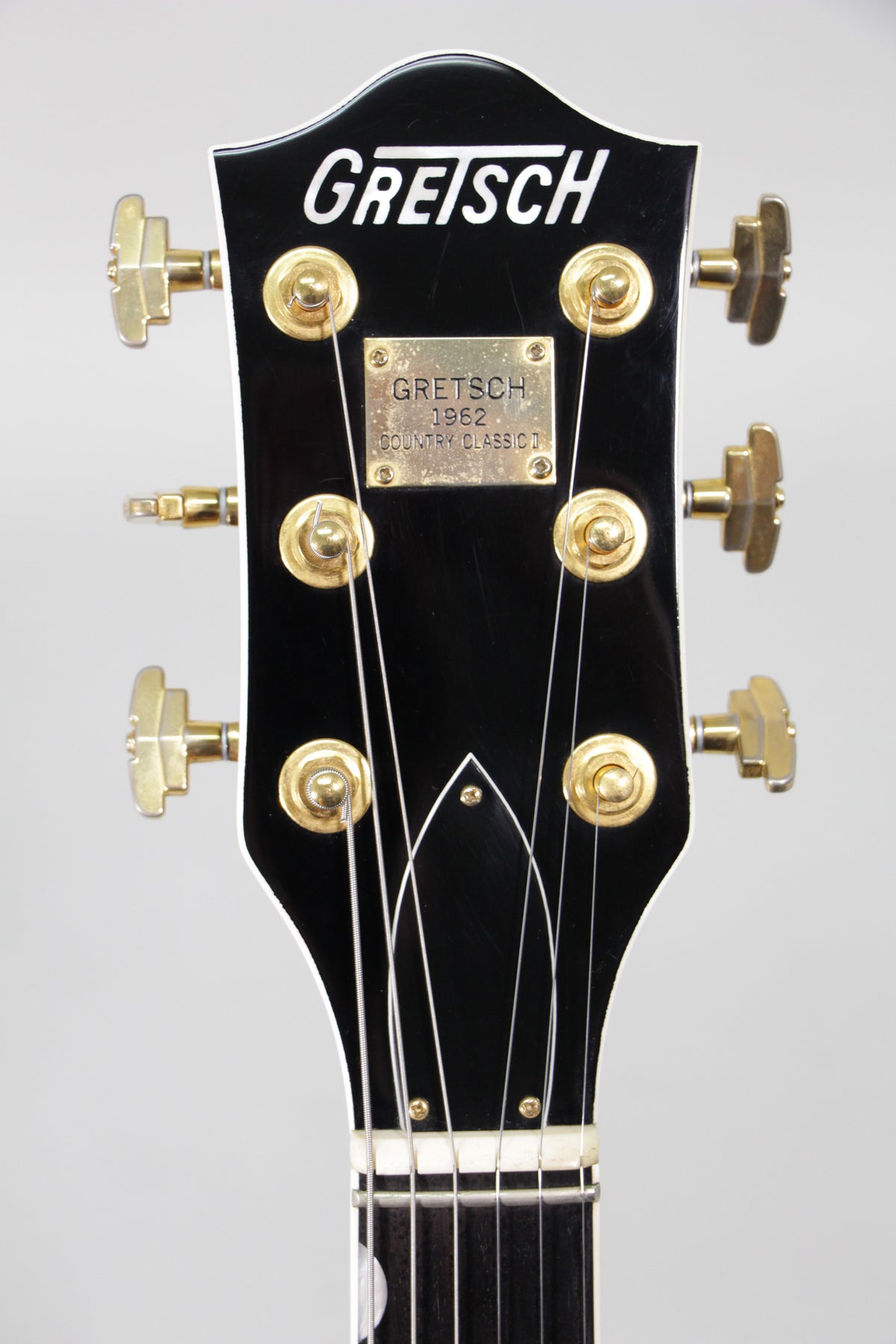 Close-up of the black headstock with gold tuners and a gold plaque, showing some light wear and string marks.