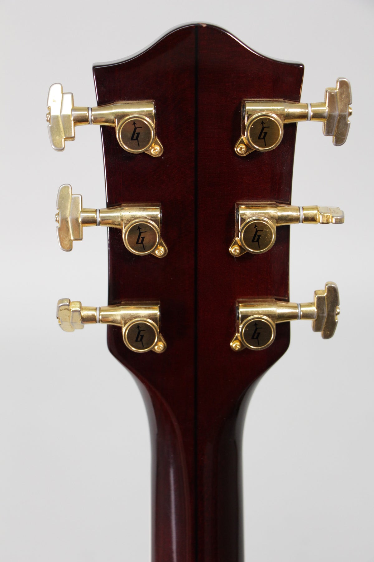 The back of the guitar's dark cherry headstock and neck, showing six gold tuners with light wear and a small chip on the top edge.