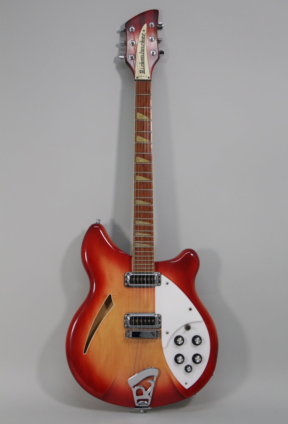 Full-length, front view of a glossy red-to-amber sunburst semi-hollow guitar with a white pickguard, chrome hardware, and five control knobs.