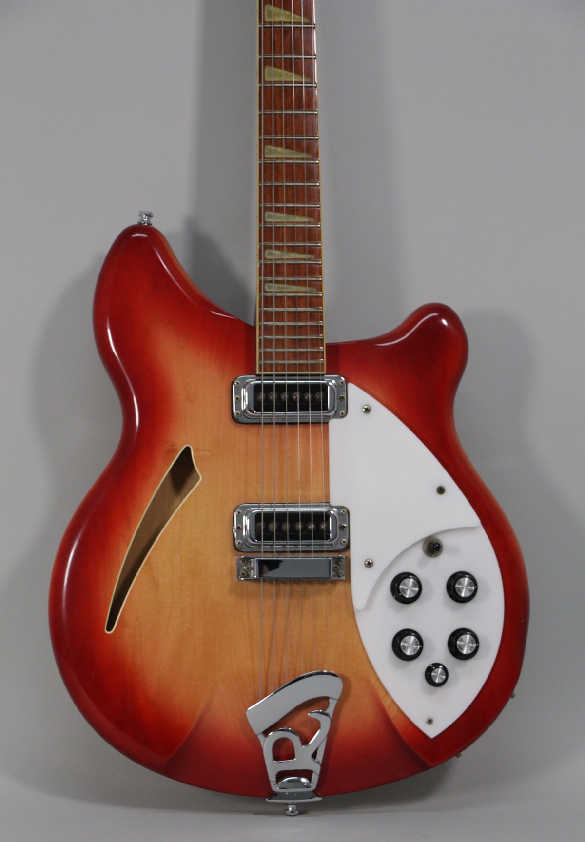 Full-frame, front view of a glossy red-to-amber sunburst semi-hollow guitar with a white pickguard, chrome hardware, and five black control knobs.