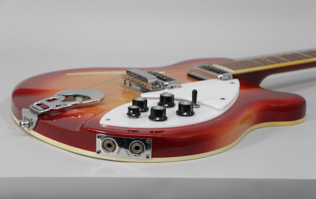 The guitar's lower body, with a red-to-orange sunburst finish, shows chrome hardware, five black control knobs, and two output jacks.