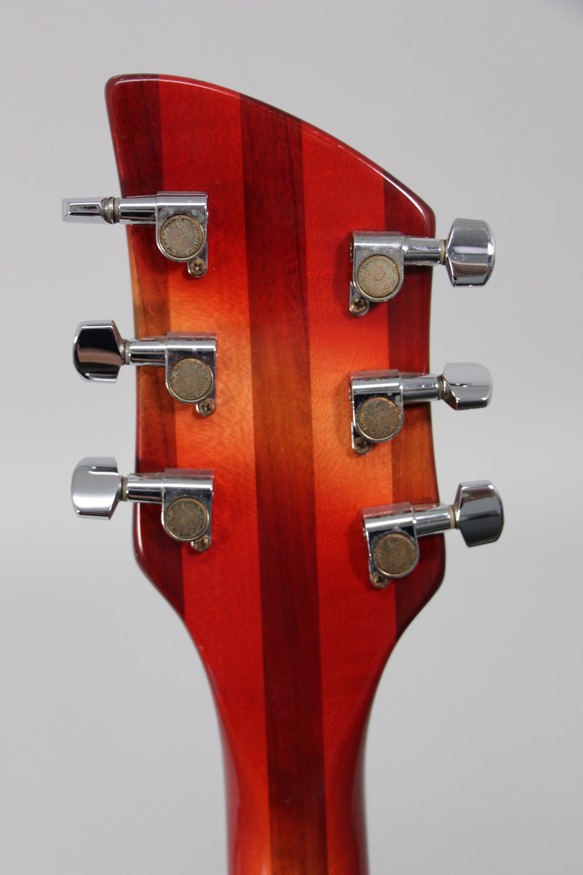The back of the guitar's headstock, showing six chrome tuners with tarnished gold-colored centers, against a striped Fireglo finish.