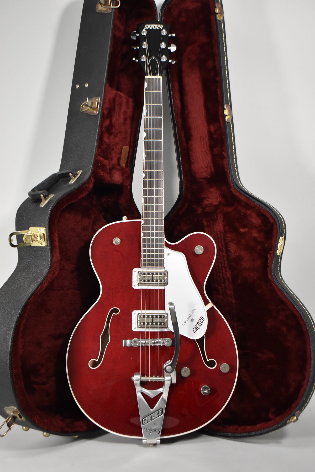 Full-length view of a cherry stain hollow-body electric guitar with white binding, f-holes, two humbuckers, and a Bigsby tremolo.