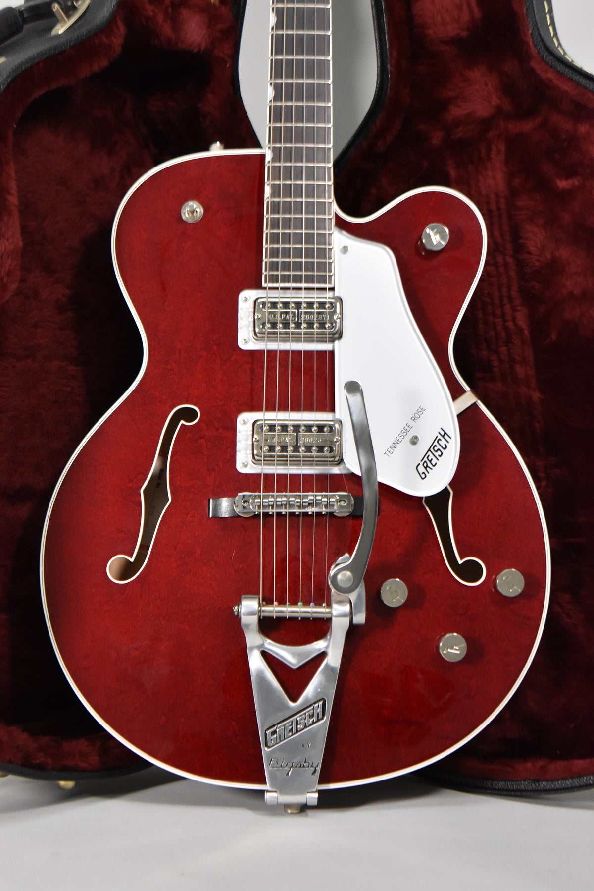 Full-body, front-facing view of a cherry red hollow-body electric guitar with a white pickguard, chrome hardware, and f-holes.
