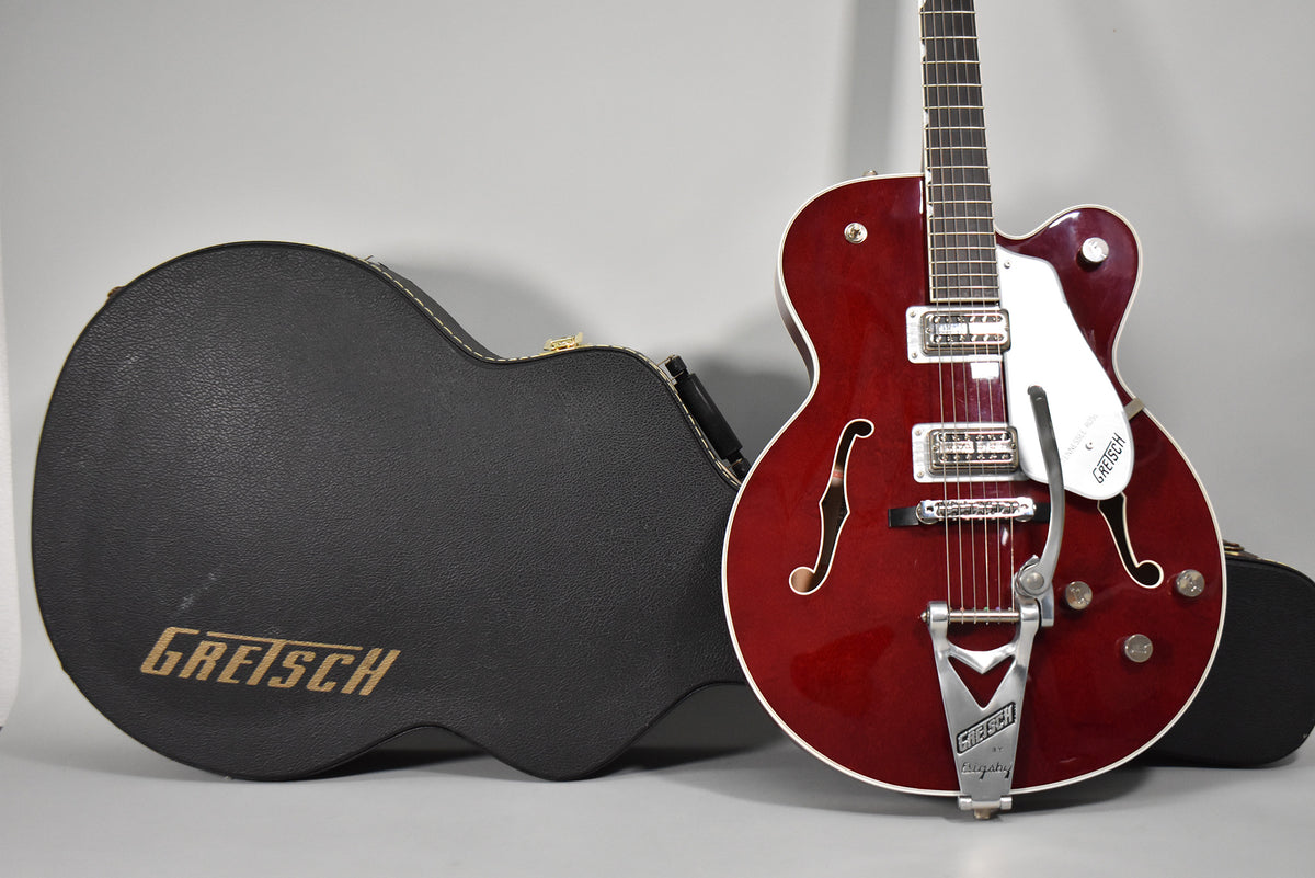 Cherry red hollow body electric guitar with white binding, f-holes, chrome hardware, Bigsby tremolo, and a black hard case.