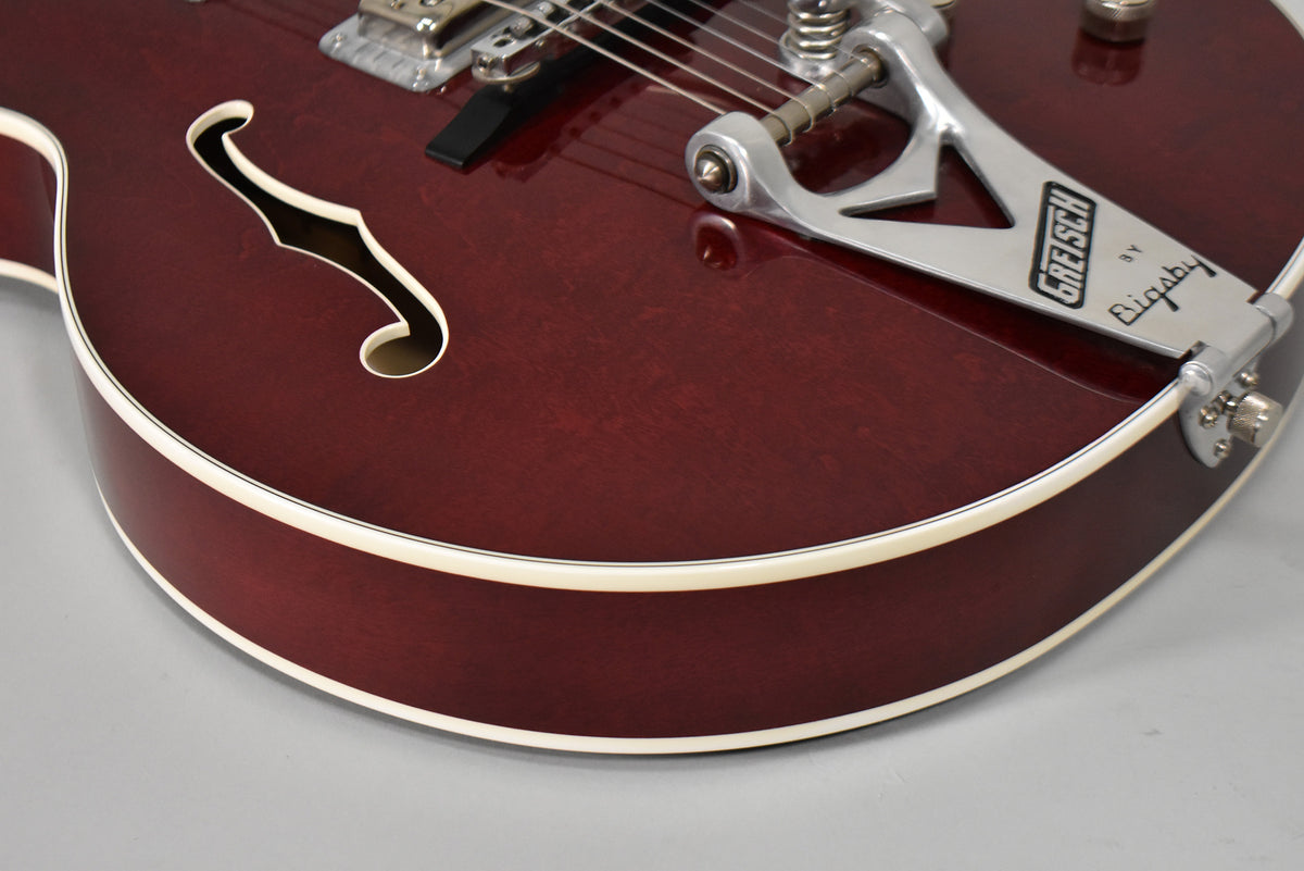 Close-up of the cherry-stained hollow body, showing the f-hole, chrome Bigsby vibrato, and cream binding along the top and side.