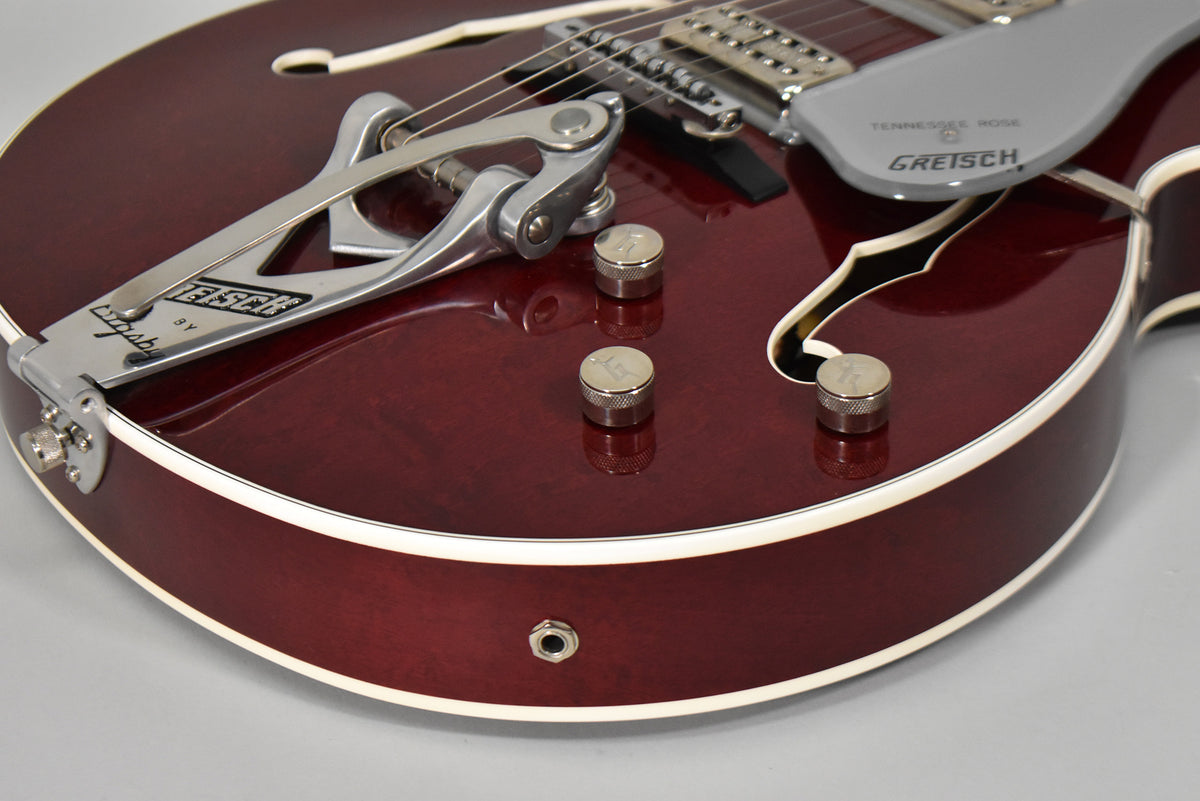 Close-up of the cherry-stained guitar body, showing the Bigsby tremolo, four chrome knobs, and output jack.