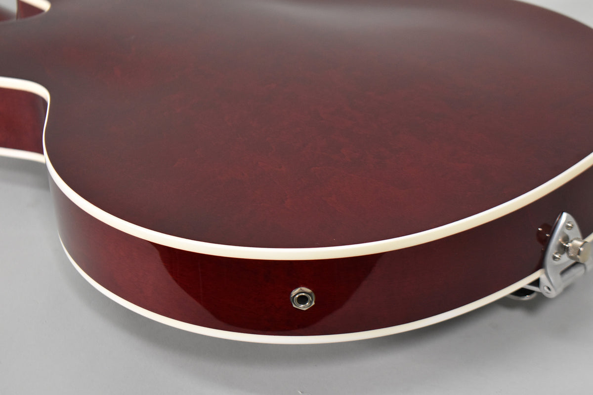 The lower bout of a cherry stain hollow body guitar, showing the output jack and a strap button.