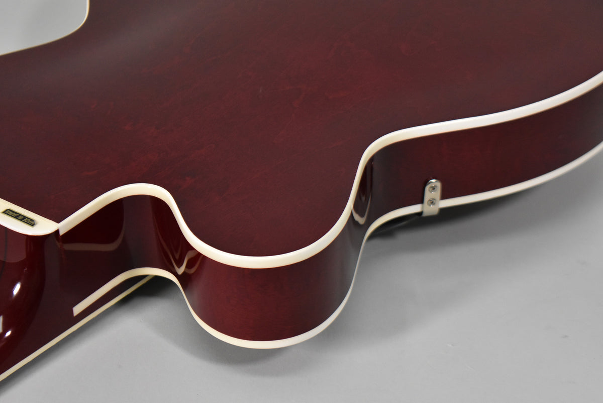 The lower bout of the cherry stain hollow body guitar, showing the white binding and a strap button on the side.