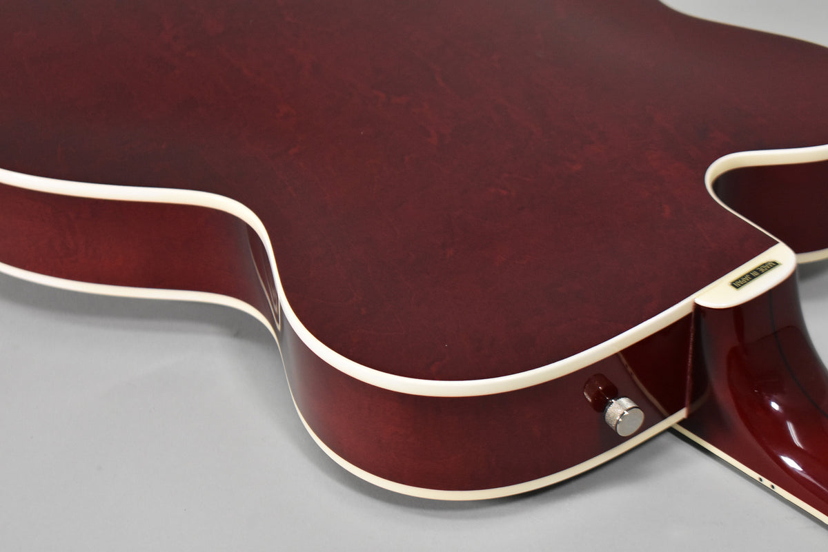 Close-up of the guitar's lower bout and cutaway from the back, showing the cherry stain finish, cream binding, and strap button.
