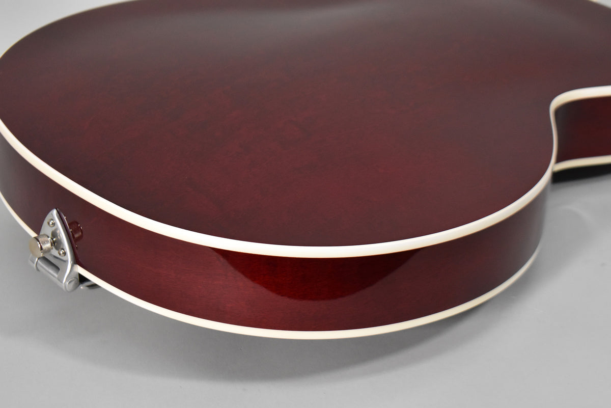 Close-up of the cherry stain guitar's lower bout, showing the glossy finish, cream binding, and a chrome strap button with light wear.