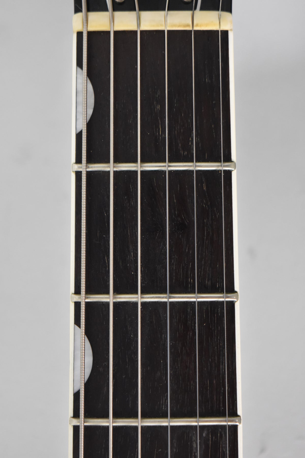 Close-up of the dark fretboard with 6 strings, 5 frets, and two half-moon inlays on the bass side, showing light wear on the nut.