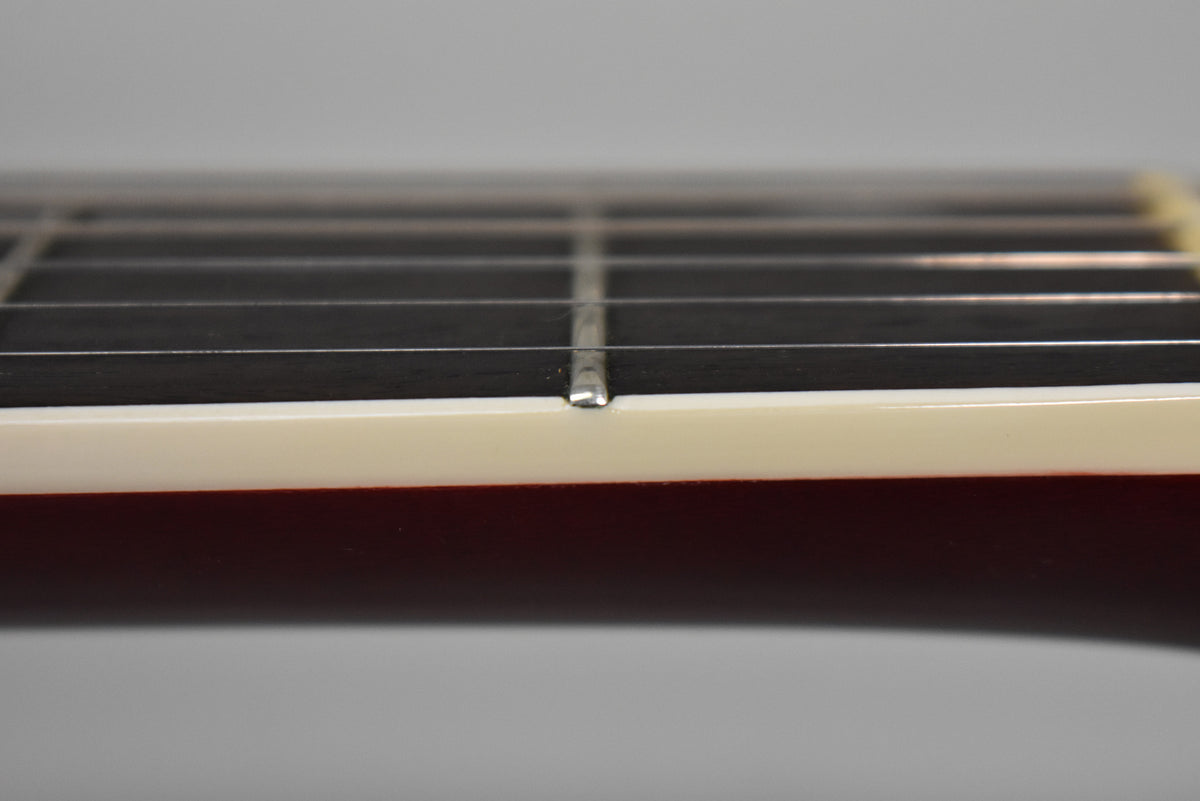 Close-up of the guitar's dark fretboard and cream binding, showing a single silver fret with minor wear, against the cherry stained neck.