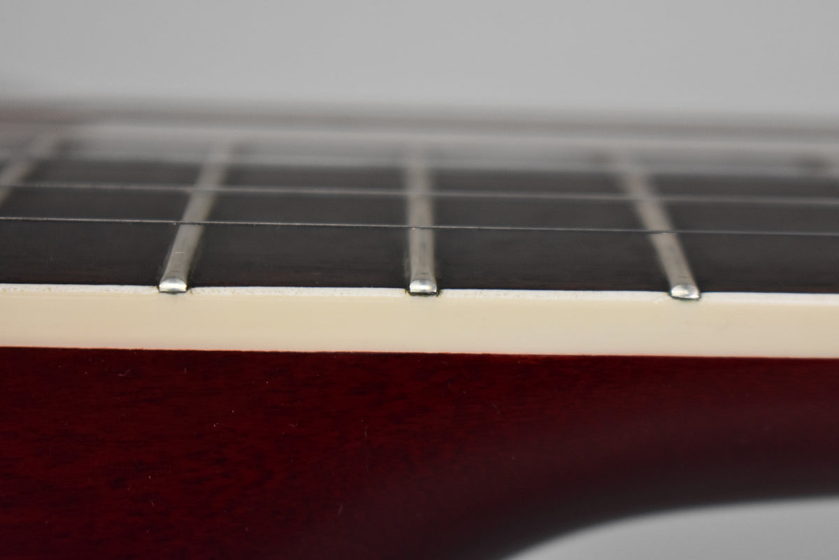Close-up of the guitar's dark fretboard and frets, with cream binding along the cherry-stained neck, viewed from the side.