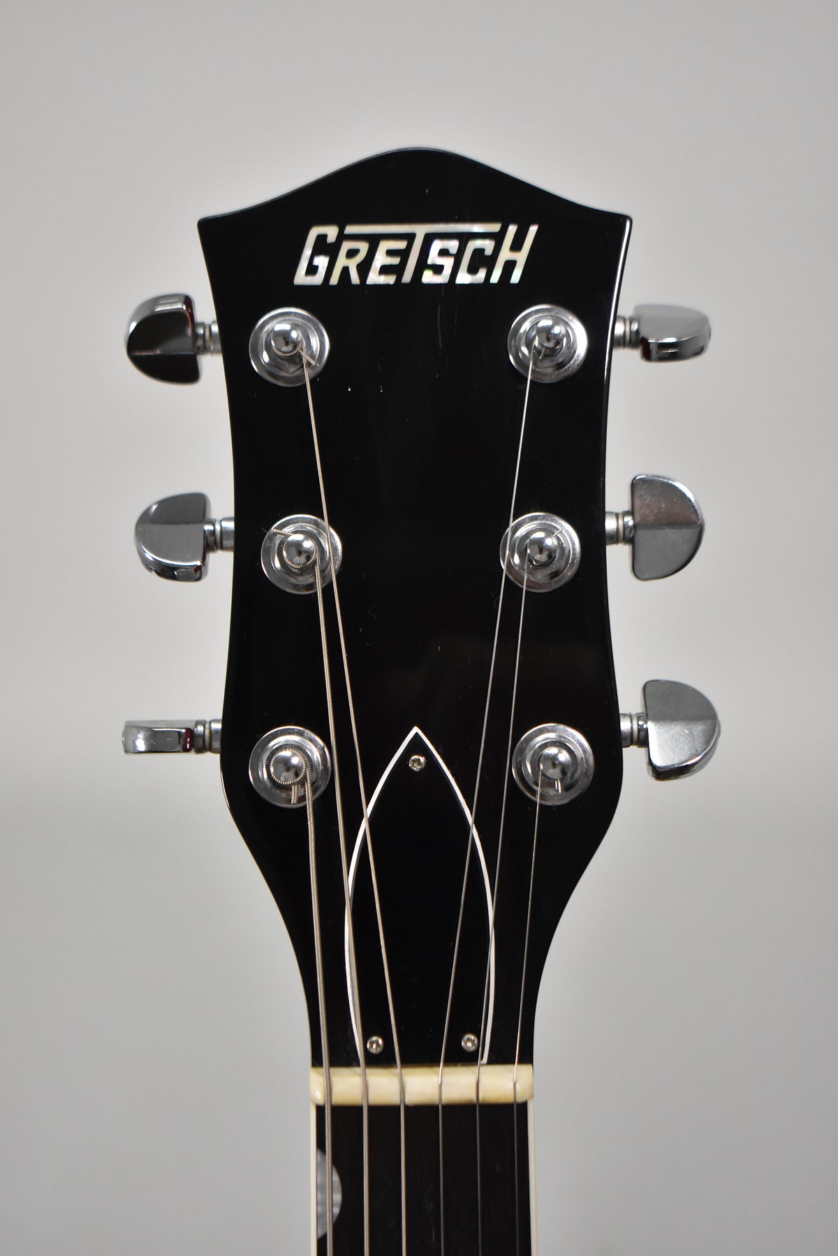 Close-up of the black headstock with six chrome tuners, a white nut, and a white truss rod cover.