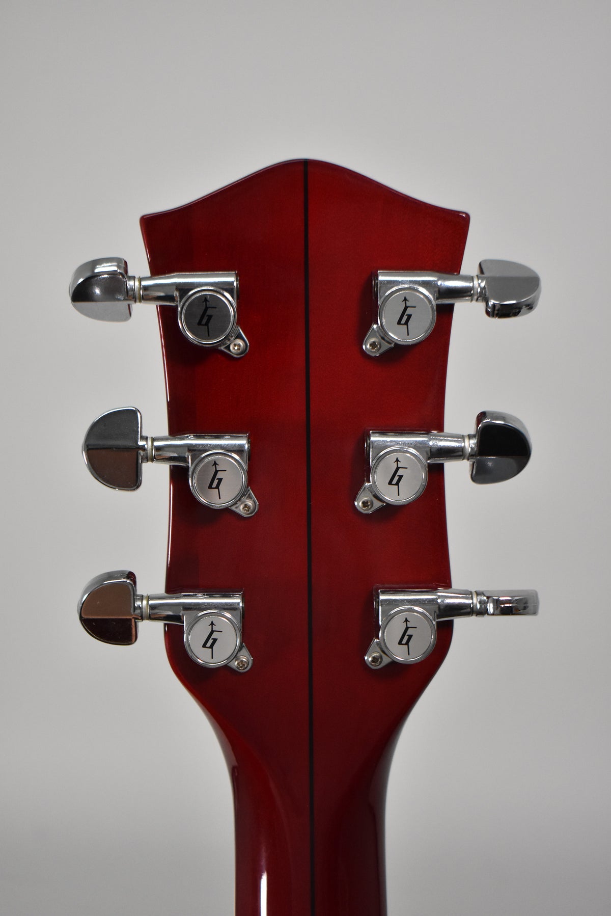 The back of the cherry-stained headstock and neck, showing six chrome tuners with G-arrow buttons and a faint center seam.