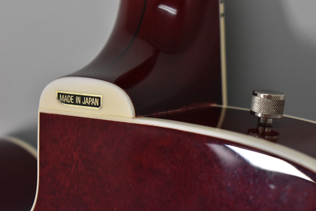 Close-up of the cherry stain guitar's neck heel and upper bout, showing a "MADE IN JAPAN" plaque and a chrome strap button.