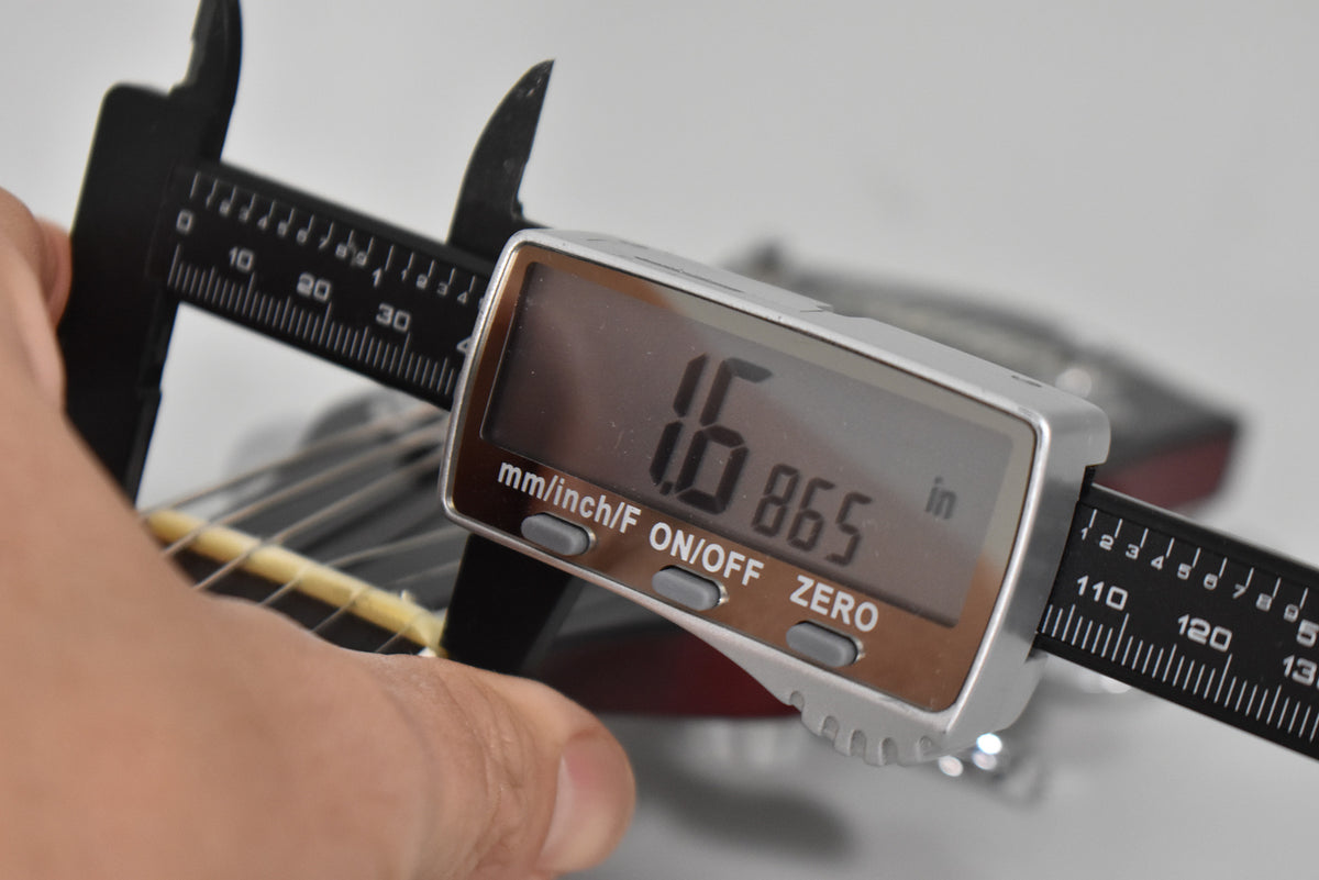 A digital caliper measures the guitar's nut width at 1.6865 inches, with a hand holding the instrument's neck.