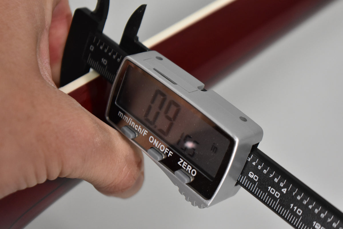 A hand holds a digital caliper measuring the guitar's cherry-stained neck, showing a reading of 0.9 inches.