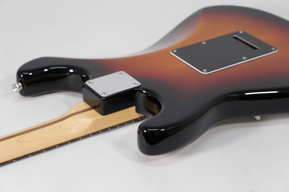The guitar's sunburst body, with a black tremolo cover and chrome neck plate, is seen from the back, angled towards the headstock.