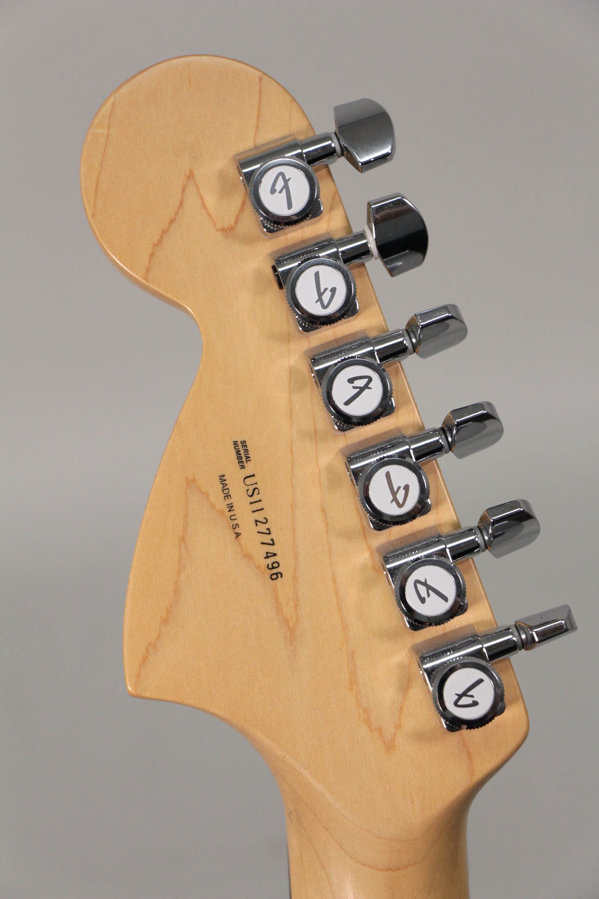 The light maple headstock, viewed from behind, features six chrome tuners with white buttons and black logos.