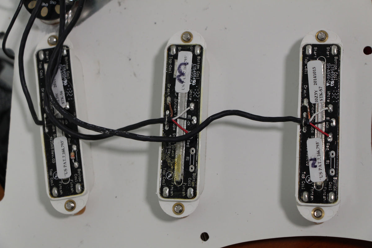 Close-up of three white single-coil pickups with black wiring and visible circuit board details, mounted on a white pickguard.