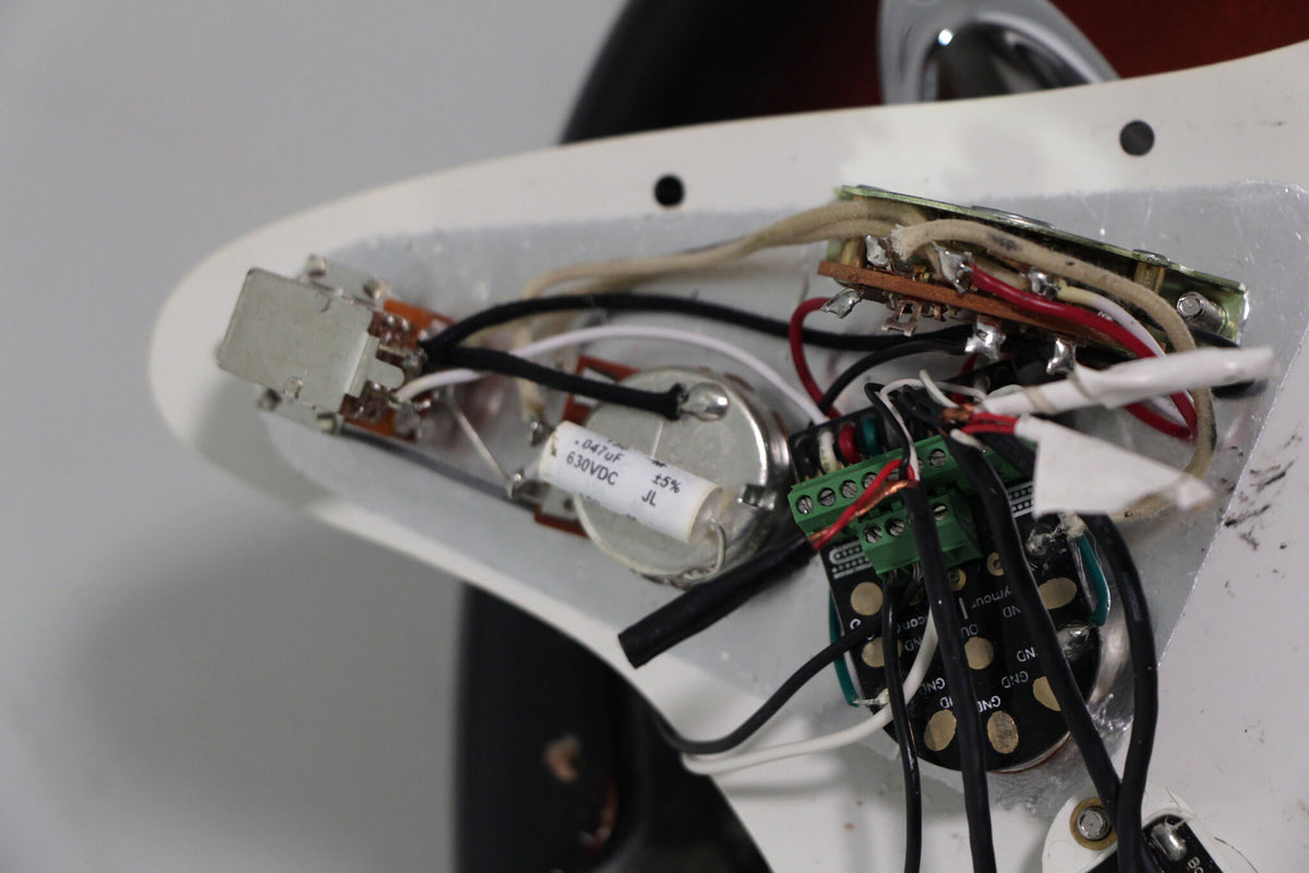 Close-up of the guitar's internal wiring, showing a white capacitor, various colored wires, and solder joints on a white pickguard.