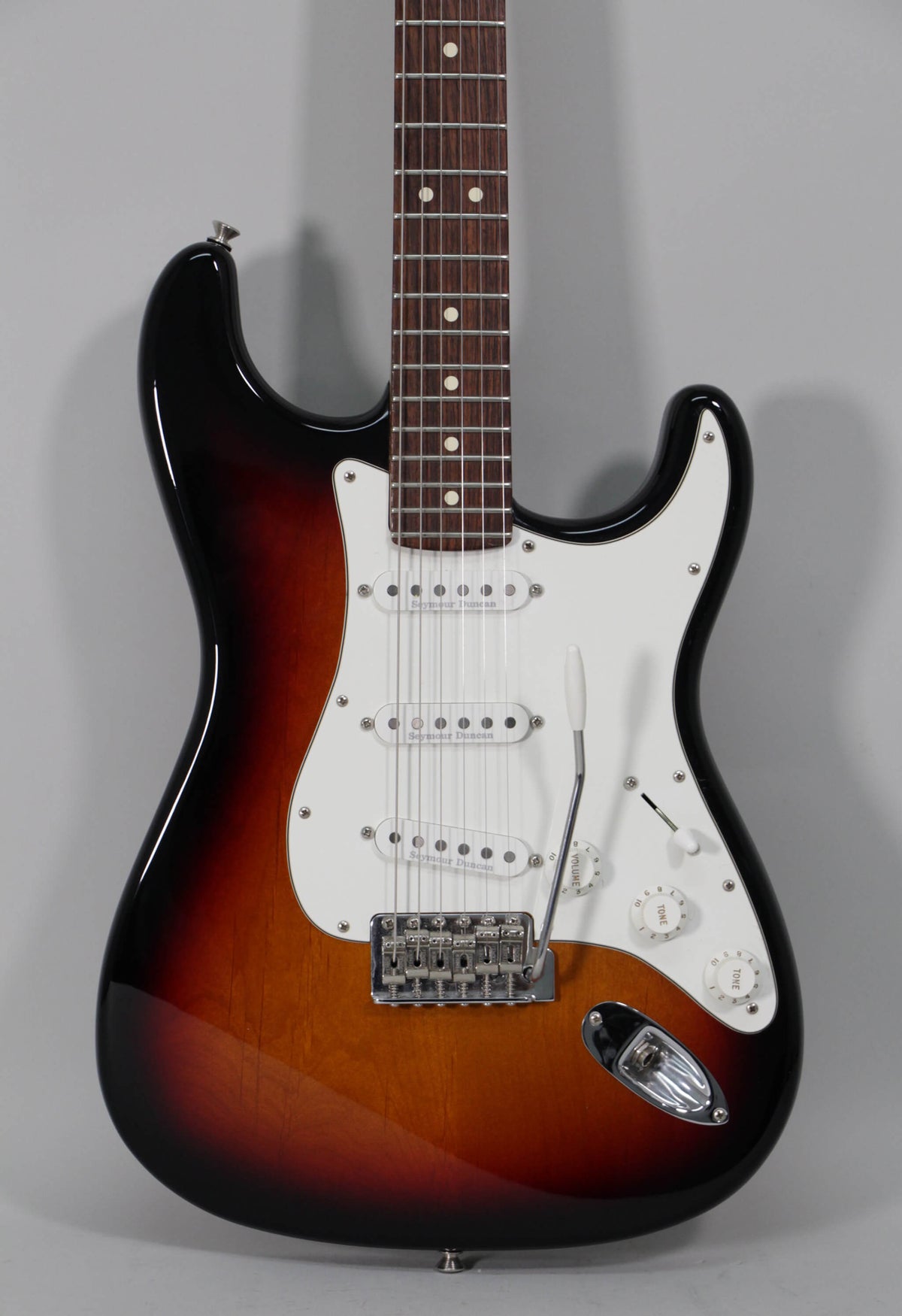 The sunburst Stratocaster is shown from the front, featuring a white pickguard, three single-coil pickups, and a tremolo bridge.