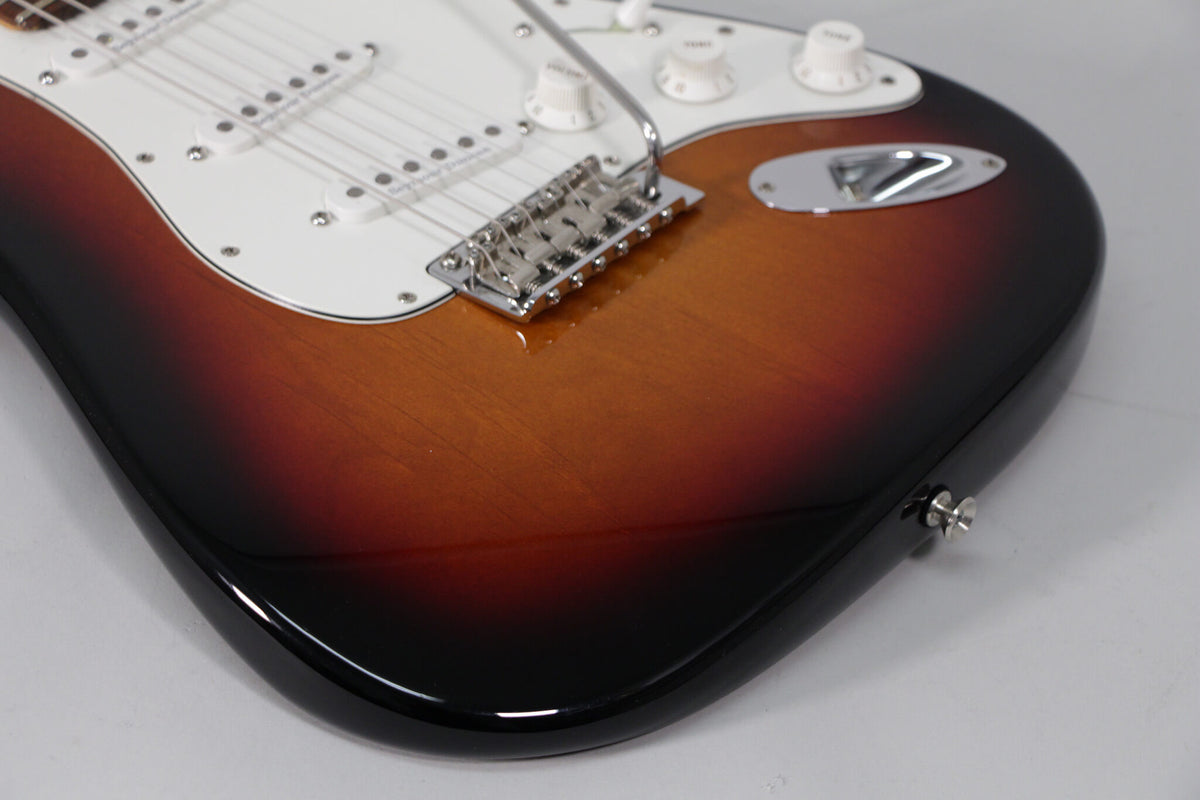 The lower bout of a sunburst Stratocaster, showing the chrome tremolo bridge, white pickguard, and output jack on the guitar's edge.