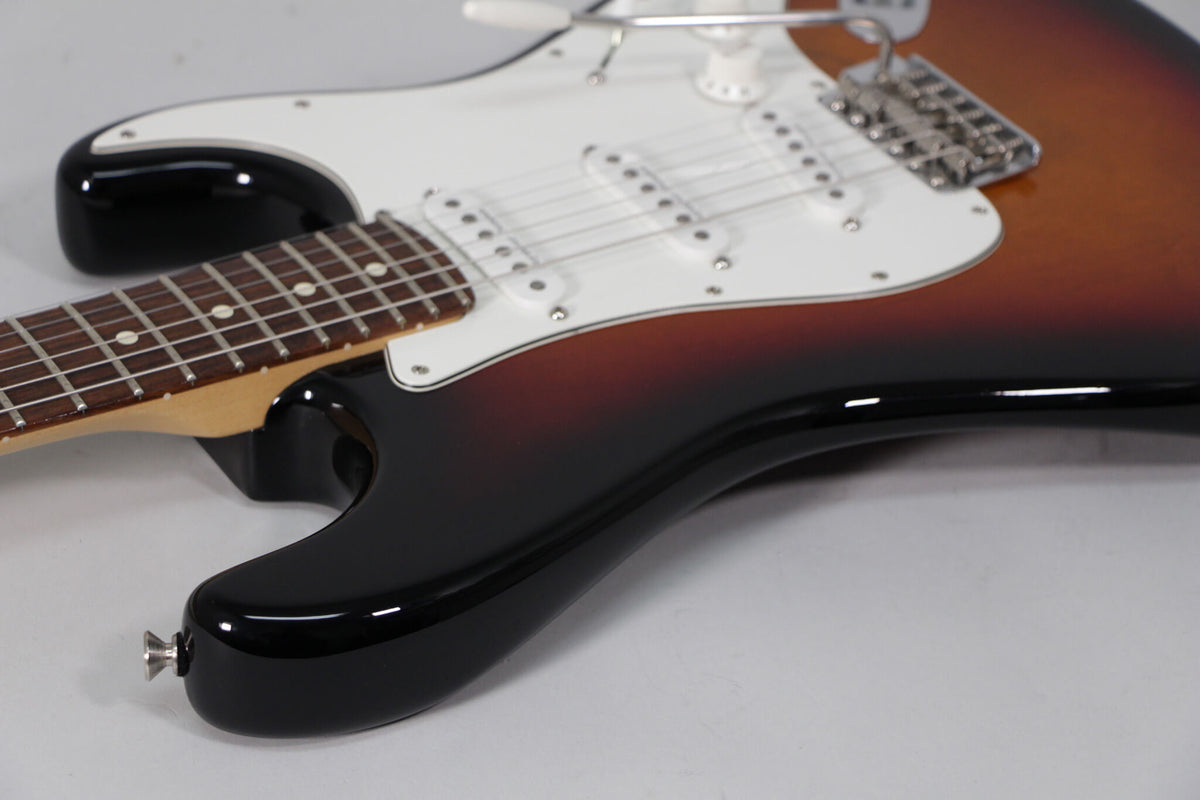 The lower body of a sunburst Stratocaster, showing the glossy black finish, white pickguard, three single-coil pickups, and tremolo bridge.