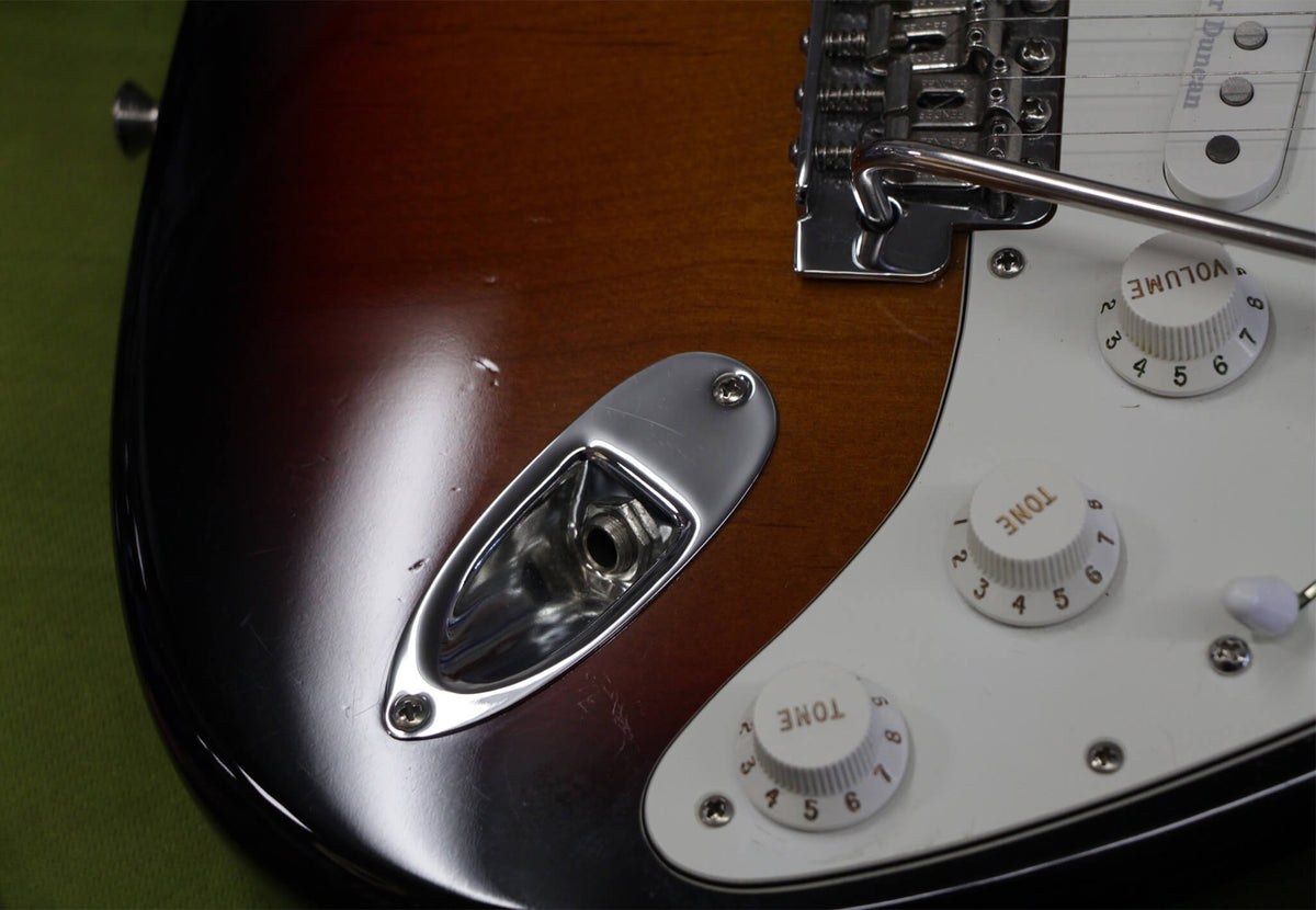Close-up of the sunburst body, showing the chrome output jack, white pickguard with three white control knobs, and some dings.