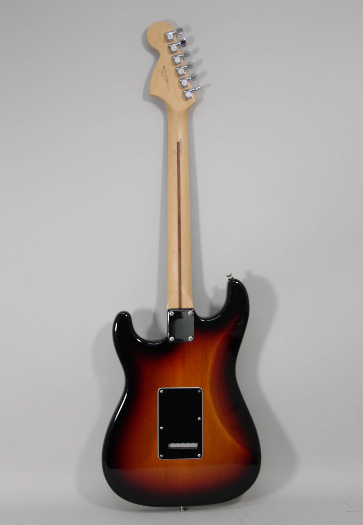 The guitar's back is shown, revealing a glossy sunburst finish, a maple neck, and a black tremolo cover.