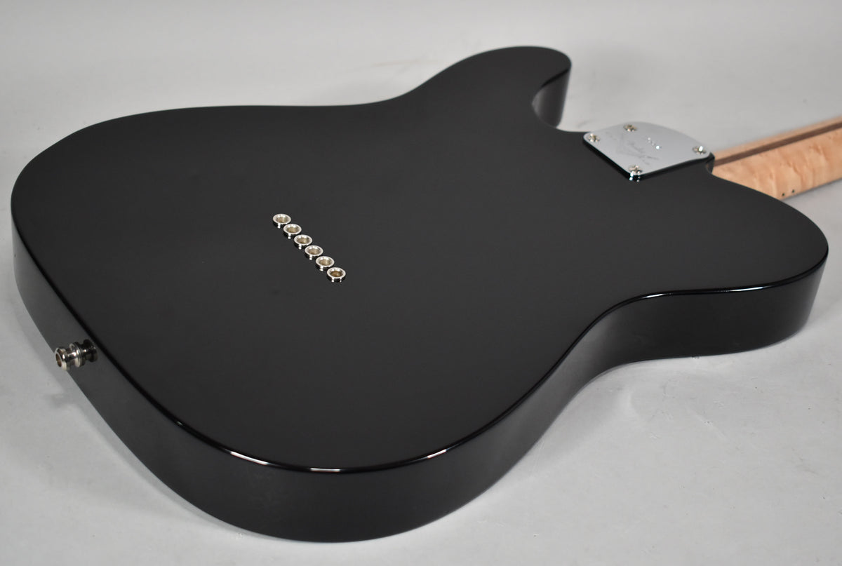 The guitar's matte black back is angled, showing six chrome string ferrules, a chrome neck plate, and a light wood neck.
