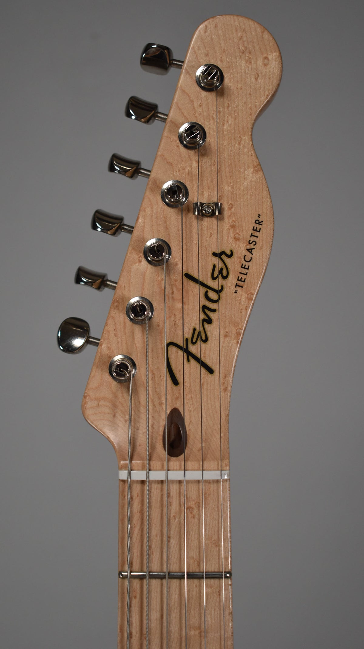 Close-up of the light wood headstock with birdseye figuring, showing six chrome tuners and a dark wood string tree.
