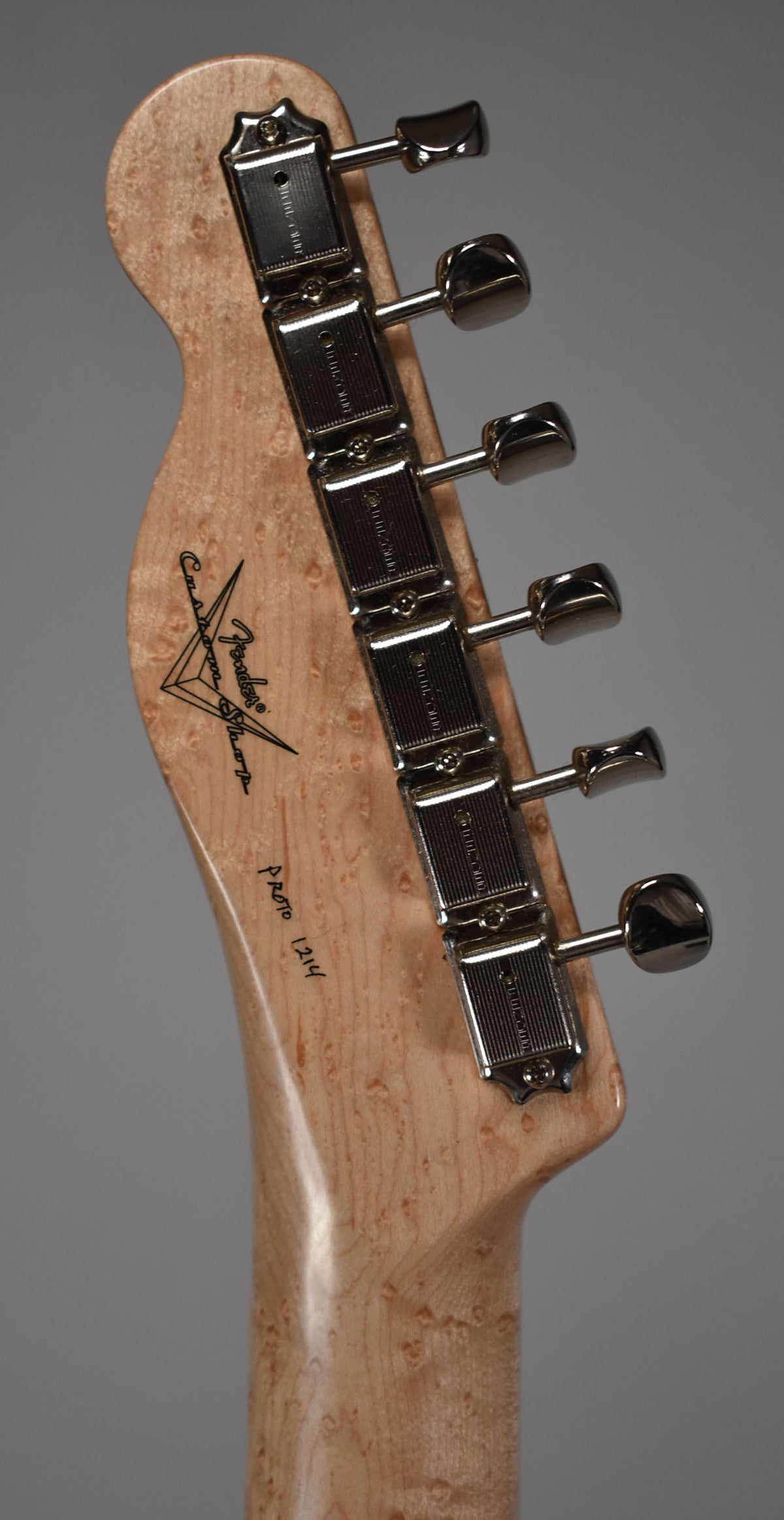 Close-up of the light wood headstock and neck, showing six chrome tuners and a dark "Custom Shop" logo.