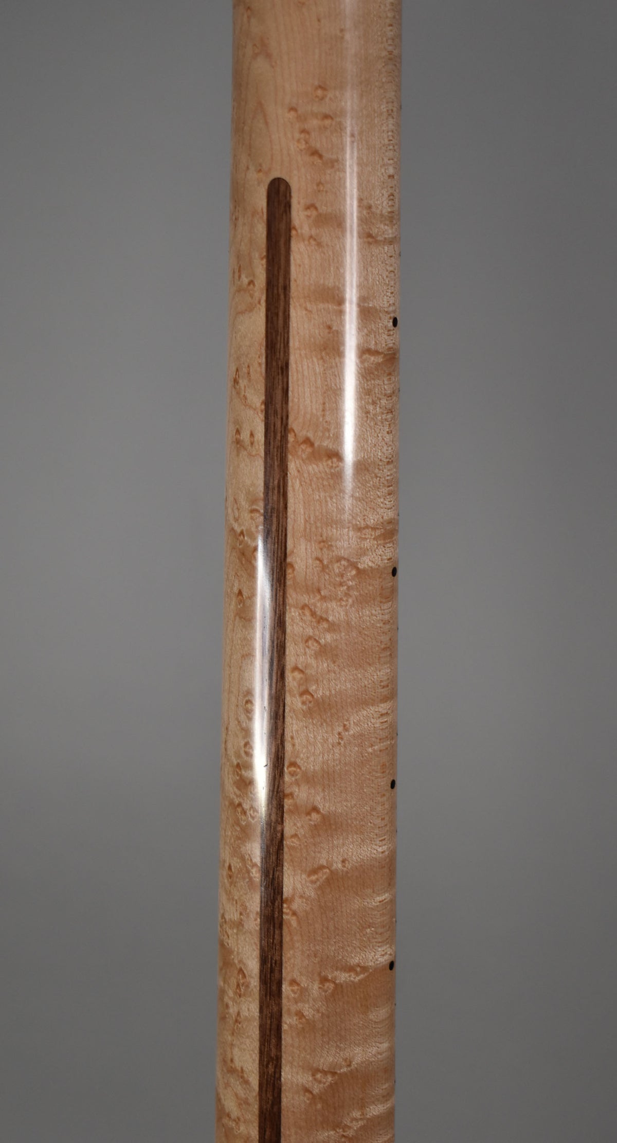 The guitar's birdseye maple neck, with a dark wood skunk stripe, is shown from the back, revealing a glossy finish and dark side dot markers.