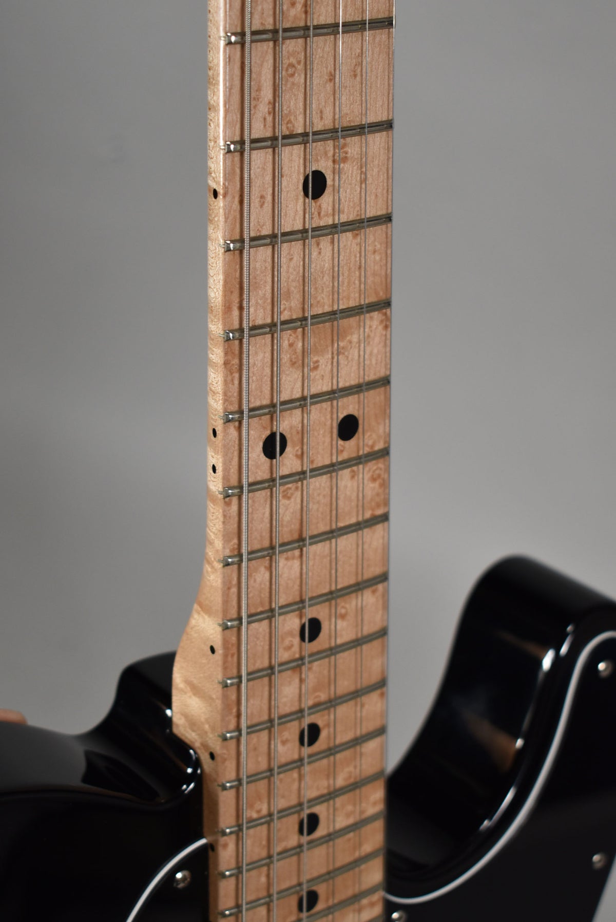 Close-up of the birdseye maple fretboard with black dot inlays, showing the neck joint and part of the glossy black body.