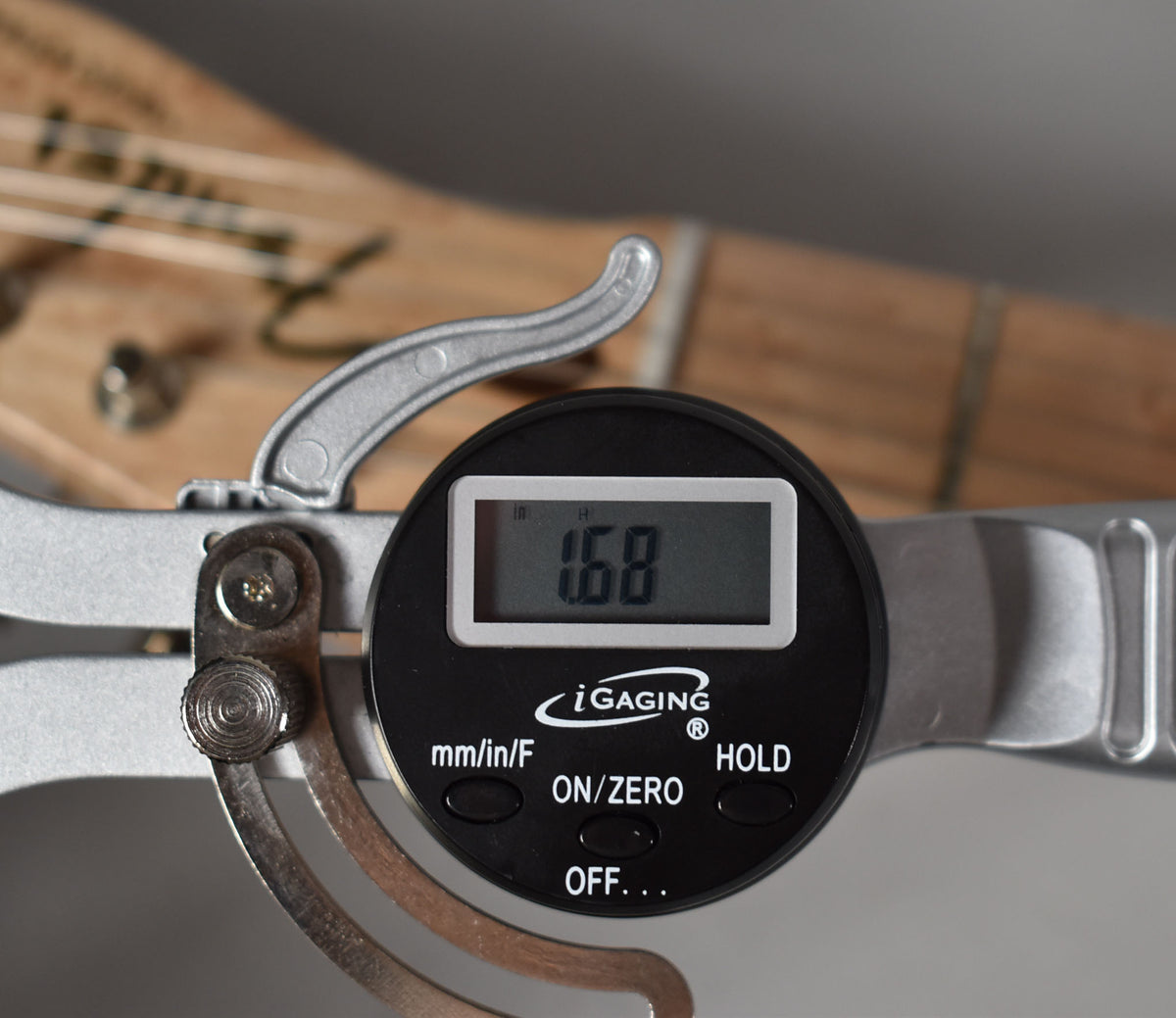 A digital caliper measures the guitar's action at 1.68mm, showing the birdseye maple fretboard and strings.