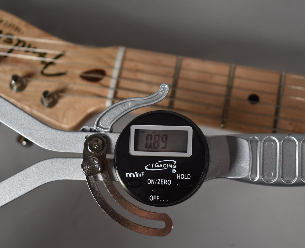 A digital gauge measuring the fret height at 0.89mm on the light wood fretboard, with the headstock visible in the background.