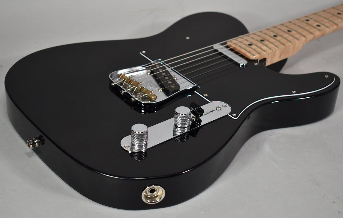 The black Telecaster body is angled, showing the glossy finish, chrome bridge with brass saddles, two knurled chrome knobs, and a black pickguard.