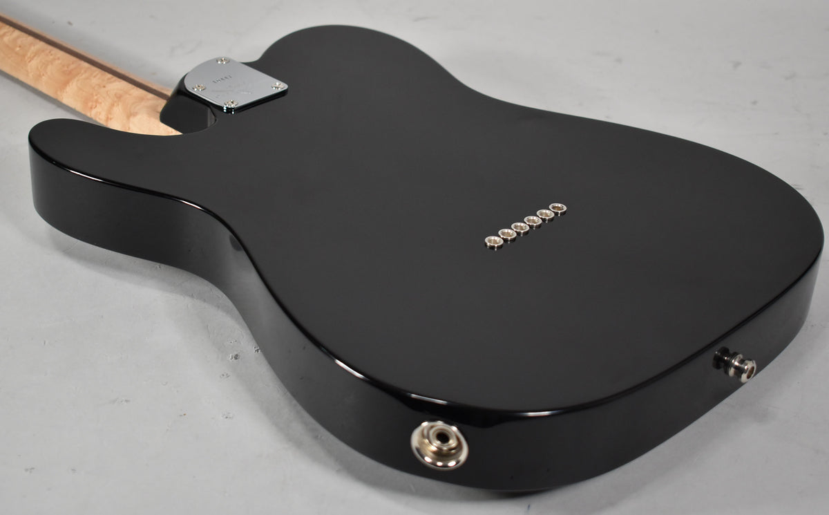 The back of a glossy black Telecaster body, angled from the neck joint, shows six string ferrules and a chrome output jack.