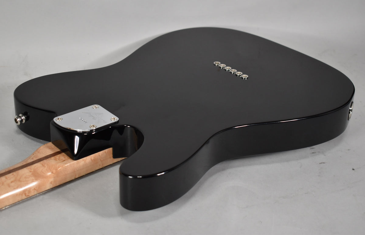 The guitar's glossy black body is seen from the back, angled left, revealing a birdseye maple neck and six string ferrules.