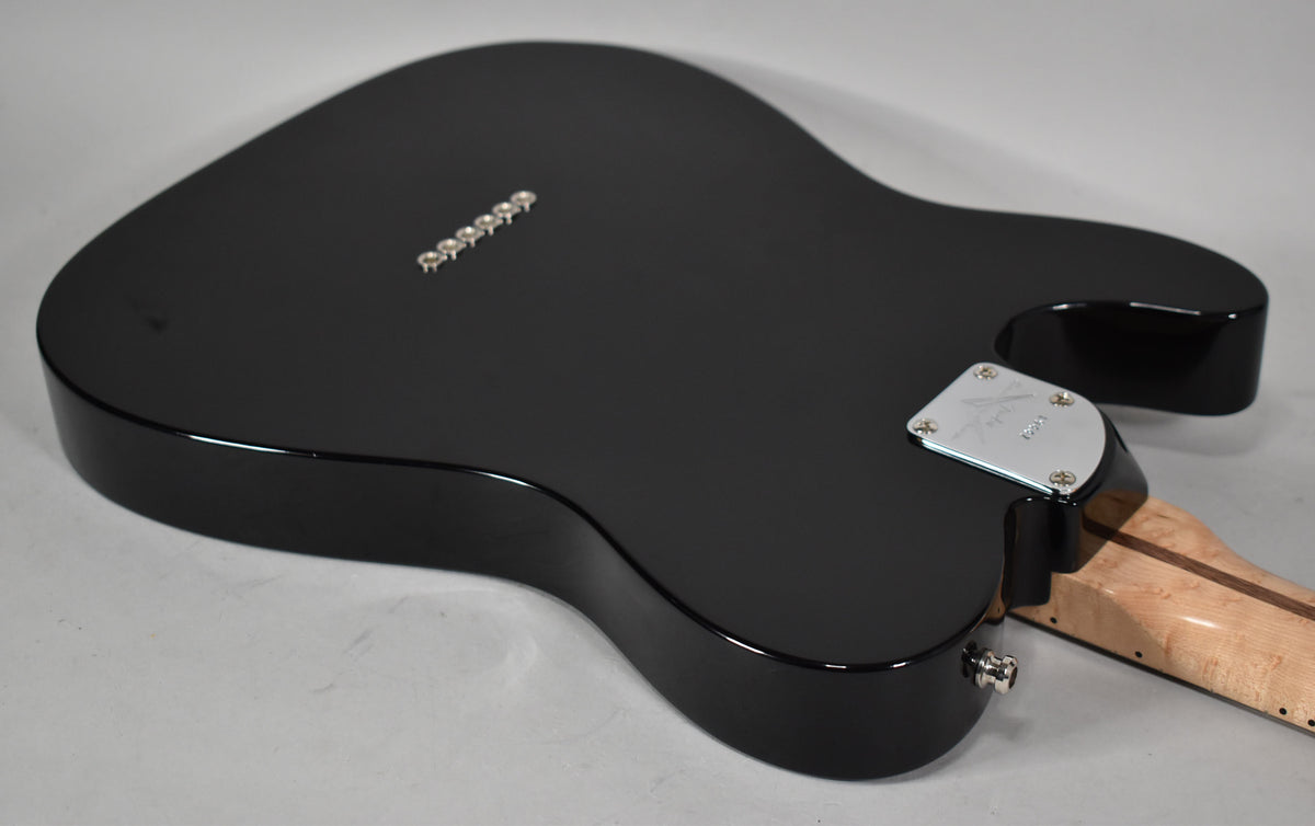 The guitar's glossy black body is viewed from the back, showing six string ferrules, a chrome neck plate, and a birdseye maple neck.