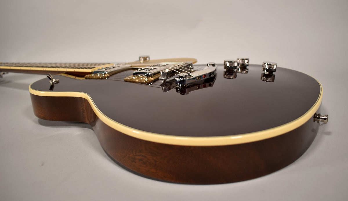 The dark brown electric guitar's body and neck are visible from the side, with chrome hardware and cream binding.