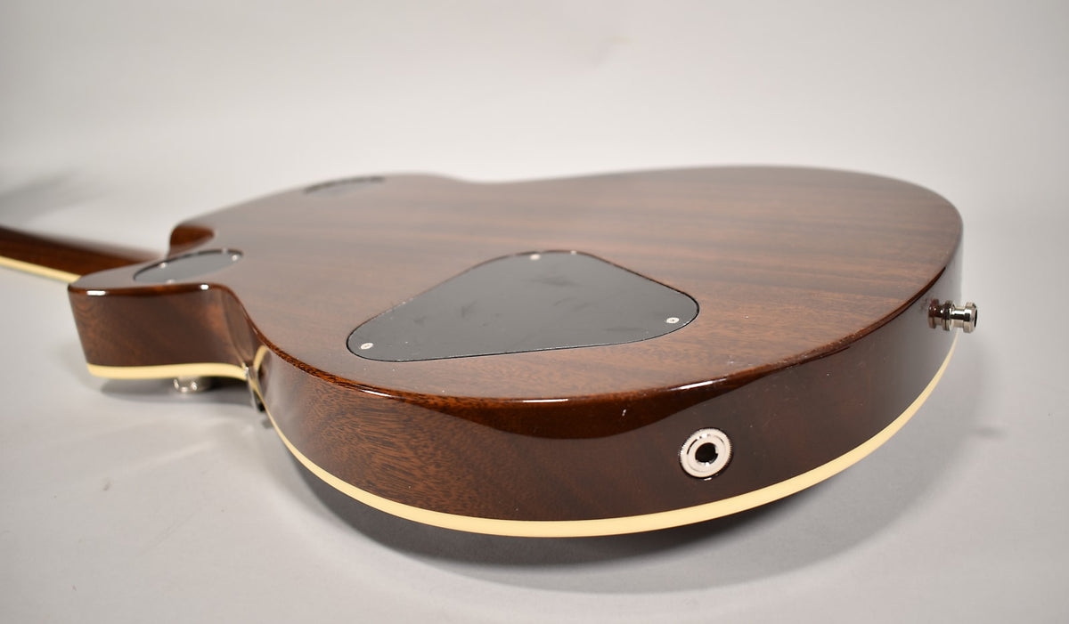The guitar's dark brown back is angled, showing the input jack, strap button, and a black control cavity cover.