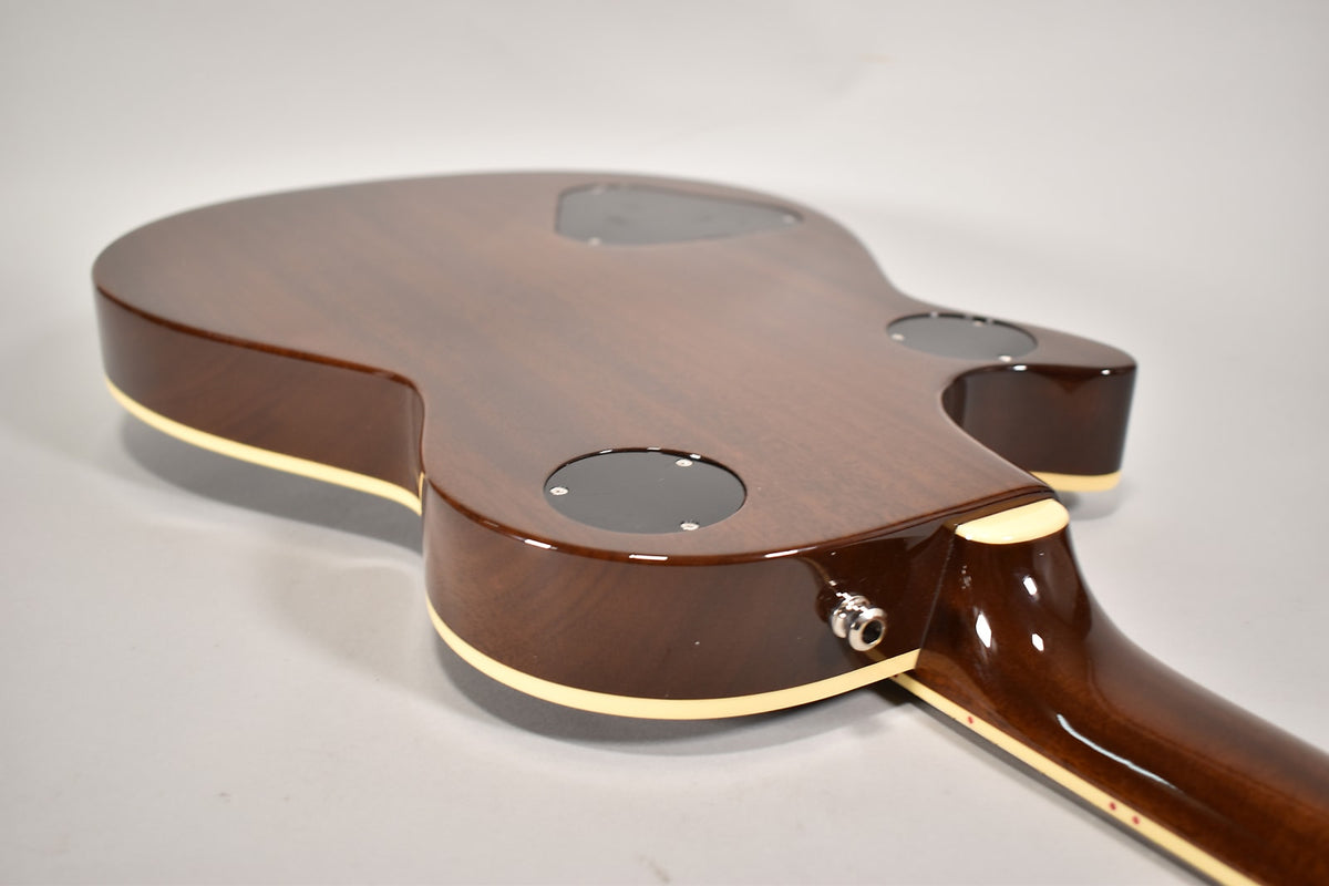 The guitar's dark brown body, with cream binding, is shown from the back, revealing control cavity covers and the input jack.