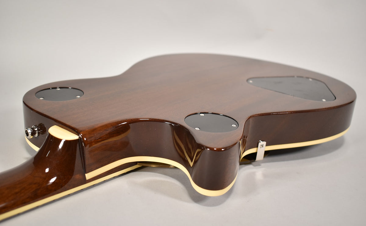 The guitar's dark brown back and neck are visible from the side, with cream binding and three black control plates.