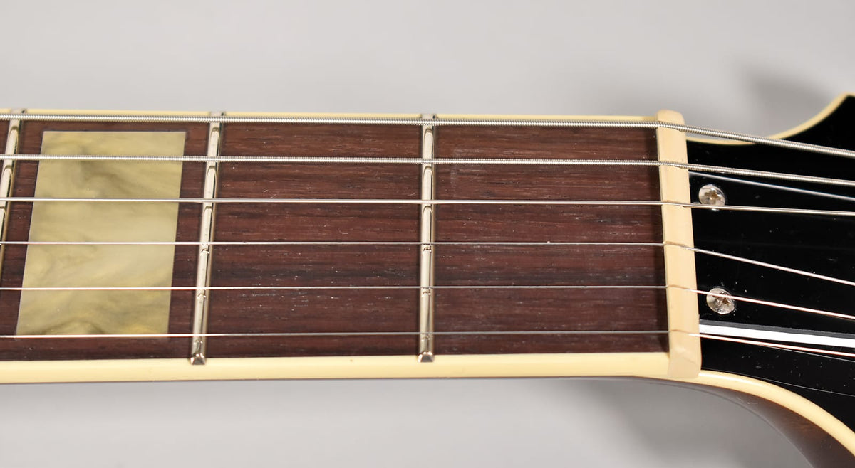 Close-up of the dark rosewood fretboard with cream binding, showing the first few frets, a pearloid block inlay, and the nut.