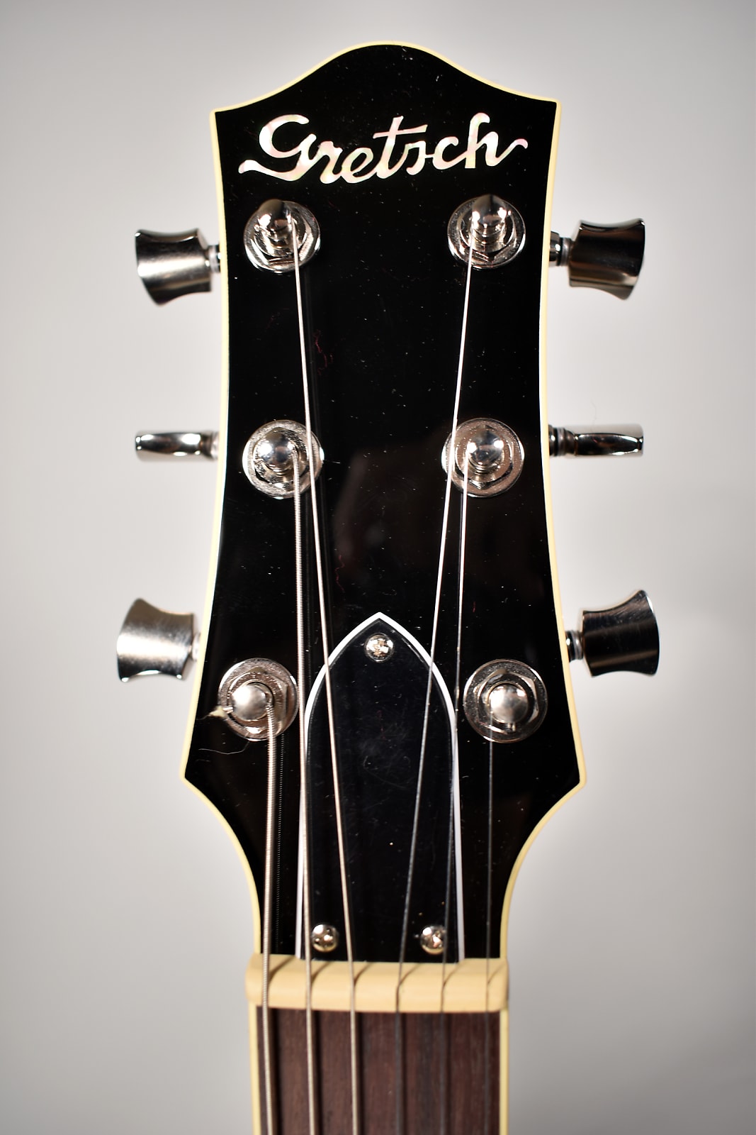 Headstock with black gloss finish, cream binding, and six chrome tuning pegs; the nut and fretboard are visible below.